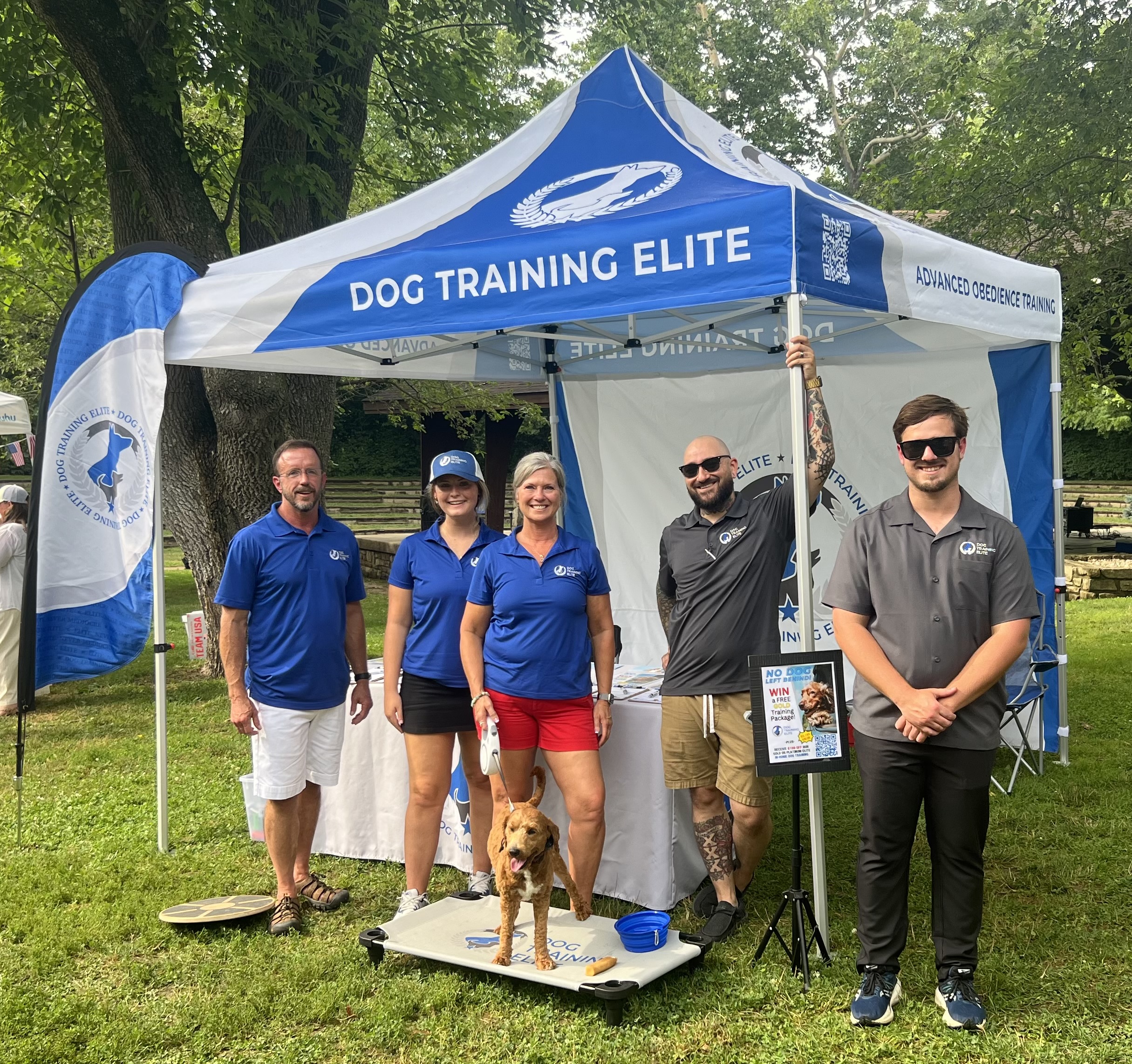 A well trained dog and their owner posing in front of a Dog Training Elite wall.